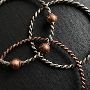 May include: Three silver and copper bracelets with twisted rope designs and copper beads.