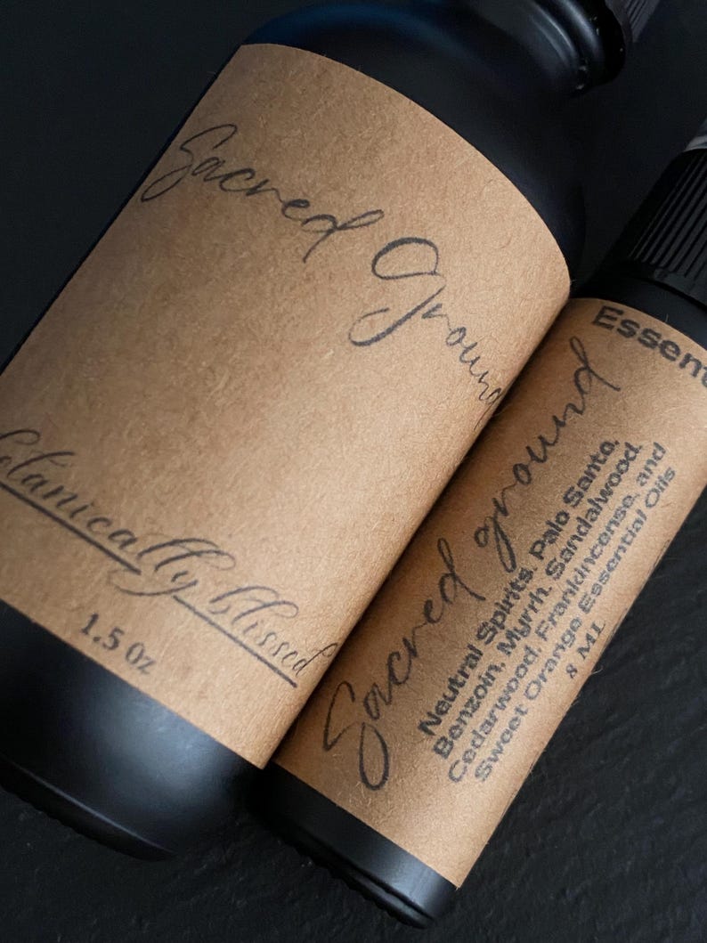 Pode incluir: Duas garrafas pretas de &oacute;leo essencial com r&oacute;tulos castanhos. Os r&oacute;tulos dizem "Sacred Ground" em it&aacute;lico. Uma garrafa tem 1,5 oz, a outra 8 ml. Ingredientes: Palo Santo, Benjoim e &oacute;leos essenciais de laranja doce.