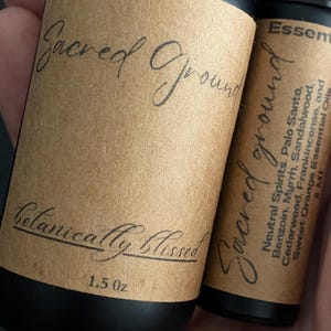 Pode incluir: Duas garrafas pretas de &oacute;leo essencial com r&oacute;tulos castanhos. Os r&oacute;tulos dizem "Sacred Ground" e "Botanically Blissed". Uma garrafa &eacute; rotulada 1,5 oz. A outra garrafa lista &oacute;leos essenciais.