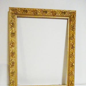 May include: Ornate gold picture frame with detailed floral and scrollwork design. The rectangular frame has a wide border and a bright, reflective finish, suitable for artwork or photographs.