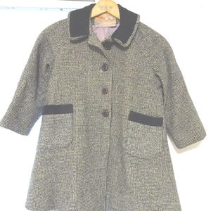 May include: A black and white tweed coat with a black collar and black trim on the pockets. The coat has a button closure and a flared skirt.