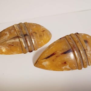 May include: Two vintage, teardrop-shaped earrings. The earrings are a marbled amber color with dark brown and white streaks. Each earring has three horizontal, silver-colored bands across the top.