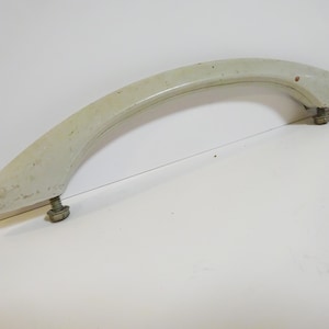 May include: A white plastic handle with two silver screws. The handle is curved and has a smooth surface.