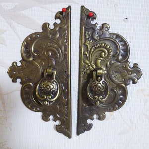May include: Two ornate brass door pulls with intricate floral designs. Each pull has a ring handle and a decorative floral accent.