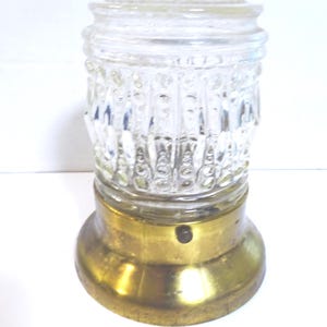 May include: A vintage clear glass light fixture with a textured, cylindrical shade and a brass base. The glass shade has a decorative pattern and a small, rounded top. The brass base is circular and slightly flared.