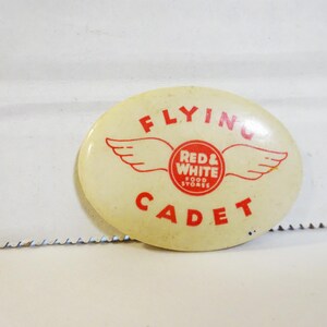 May include: White oval button with red text that reads "Flying Cadet" and a red and white circle with the text "Red & White Food Stores" and a pair of red wings.