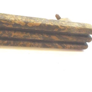 May include: Close-up of a stack of three weathered, rectangular wooden planks. The planks have a mottled brown and tan pattern, with a rough, textured surface. A small, rounded wooden peg is visible on the top plank.
