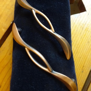 May include: Two copper-colored cabinet door pulls with a unique, twisted design. The pulls are on a black velvet background.