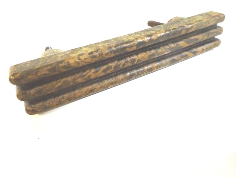 May include: A weathered, rectangular drawer pull with a layered design. The hardware features a mottled brown and gold finish, suggesting an antique or vintage aesthetic. The pull has a small, rounded handle.