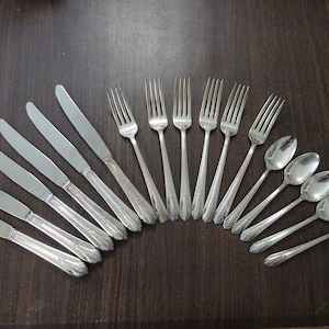 May include: A set of silverware, including knives, forks, and spoons, arranged in a semi-circle on a dark brown wooden surface. The silverware is made of polished silver and has an ornate design.