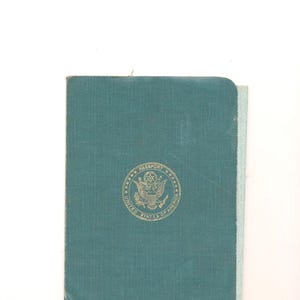 May include: A teal United States passport with a gold embossed seal. The passport has a textured cover and is slightly worn. The seal reads "PASSPORT UNITED STATES OF AMERICA".