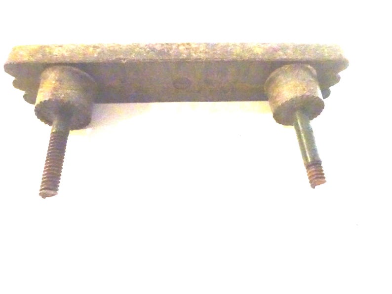 May include: A weathered, rectangular metal drawer pull with two cylindrical posts and threaded screws. The pull has decorative edges and a tarnished, aged appearance, suggesting vintage hardware.