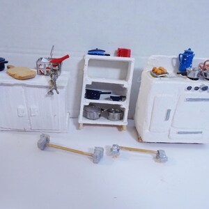 May include: A miniature white kitchen set with a cabinet, a shelf, and a stove. The set includes a variety of miniature kitchen accessories, such as pots, pans, and a milk jug.