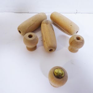 May include: A collection of unfinished wooden knobs and handles. The pieces vary in shape, including cylindrical handles and rounded knobs. Each piece has a hole drilled through it, and the wood has a natural, light brown color.