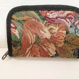 May include: A rectangular wallet with a tapestry design. The wallet features a black zipper and trim. The tapestry pattern includes shades of red, green, and beige. The wallet is approximately 5 inches wide and 4 inches tall.