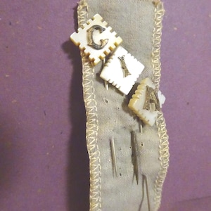 May include: A vintage pin cushion with three decorative pins spelling "CIA". The pins have white square heads with the letters in a metallic color. The pin cushion is a light gray fabric with a decorative trim and several silver pins.