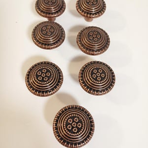 May include: Seven bronze-colored cabinet knobs with a detailed, circular design. Each knob features a central pattern of small circles surrounded by concentric rings and a short stem for attachment. The knobs are arranged on a white surface.