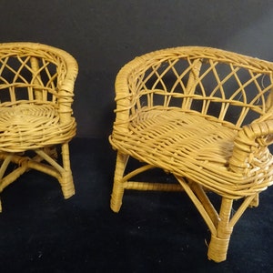 May include: Two small wicker chairs with a light brown finish. The chairs have a rounded back and a woven seat.