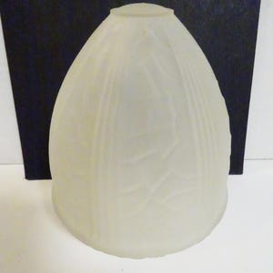 May include: A frosted glass lampshade with an egg-like shape. The off-white shade features vertical lines and a textured pattern. The lampshade has a small, rounded top and is designed to diffuse light.