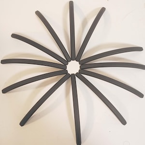 May include: A collection of dark gray, curved, stick-like objects arranged in a circular pattern, resembling a stylized sun or star. The objects are evenly spaced and radiate outwards from a central point.