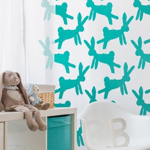 May include: A nursery with a white crib, a white chair, and a wall decorated with a teal bunny pattern. A stuffed bunny and other toys sit on a white shelf. A black and white polka dot banner hangs over the crib.