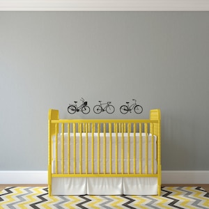 May include: A yellow crib with a white mattress and white bedding. Three black bicycle silhouettes are on the gray wall behind the crib.