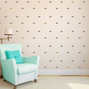 May include: A light blue armchair with a turquoise pillow sits next to a wall decorated with gray and gold cloud decals. A lamp with a beige lampshade is on the left. The room has a cream-colored carpet and walls.
