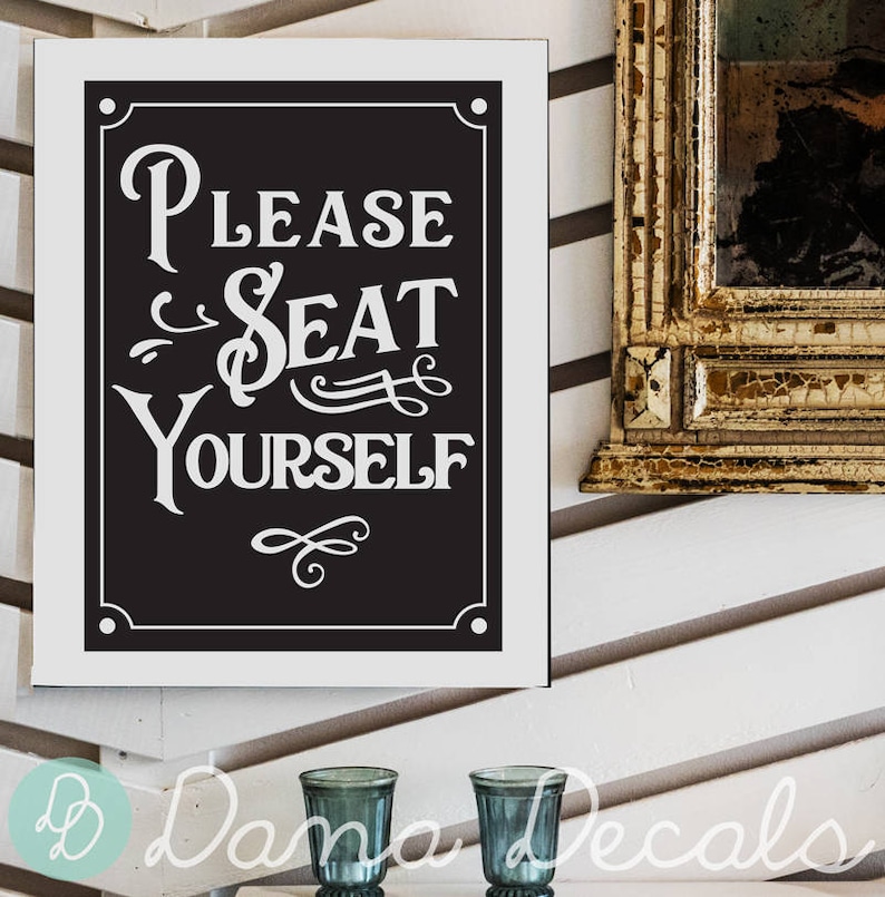 以下が含まれることがあります： 「PLEASE SEAT YOURSELF」の文字が装飾的な書体で書かれた白黒のサイン。サインは白いフレームで囲まれ、角には装飾的なアクセントがあります。白い壁に掛けられており、背景には2つの青いグラスと金色のフレームの鏡があります。
