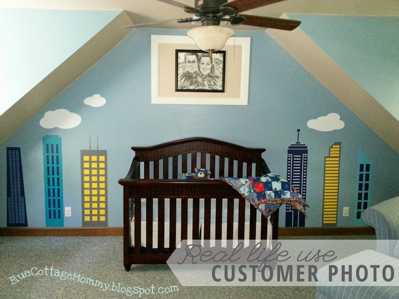 Puede incluir: Una habitaci&oacute;n de beb&eacute; con un esquema de color azul y blanco. La habitaci&oacute;n cuenta con una cuna con una colcha azul y roja, un ventilador de techo y un marco de fotos con una foto de una pareja. Las paredes est&aacute;n decoradas con un mural de ciudad con nubes blancas y edificios amarillos, azules y grises.