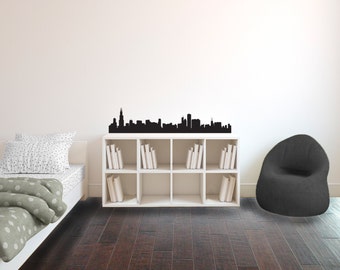Könnte beinhalten: Eine schwarze Skyline-Silhouette-Wanddekoration über einem weißen Würfelregal mit Büchern. Der Raum umfasst ein Bett mit einem gepunkteten Bettbezug und einen dunkelgrauen Sitzsack auf einem dunklen Holzboden.