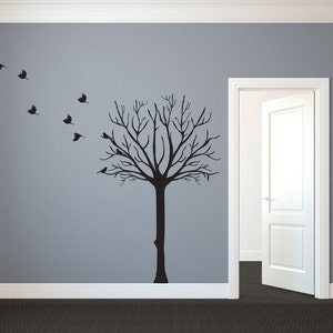 May include: A black tree wall decal with birds flying to the left. The tree has many branches and is affixed to a gray wall. A white door is open to the right, and the floor is black.