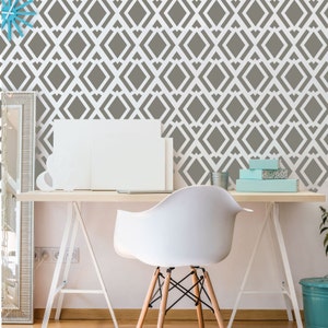 May include: A modern home office setup featuring a white desk, chair, and a geometric patterned wall. The wall has a repeating diamond design in gray and white. Decorative items include blank canvases and small blue boxes.