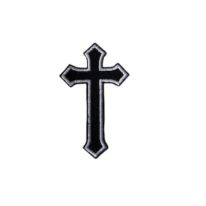 May include: A black cross patch with a pointed, stylized shape and a thin white embroidered border. The design features sharp, angular edges at the top, sides, and bottom, creating a distinct silhouette against the plain white background.