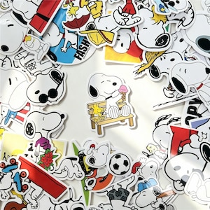May include: A collection of vinyl stickers featuring the white beagle character Snoopy in various poses and activities, including sitting on a wooden bench eating an ice cream cone, wearing sunglasses, and playing with a football.