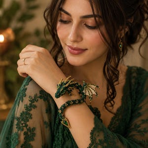 Op de afbeelding: Een flexibele armband in de vorm van een draak, gemaakt van donkergroene en gouden kralen, met een gedetailleerde kop met een groene edelsteen, textuurschubben en kleine vleugels. Het lichaam wikkelt zich om de pols en eindigt in een puntige staart.