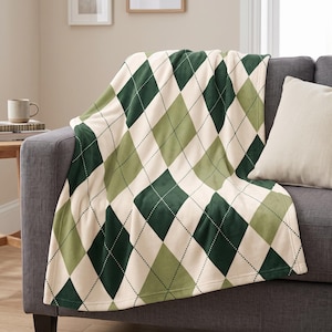May include: A soft throw blanket featuring a classic argyle pattern in shades of dark forest green, light sage green, and cream. The design consists of repeating diamond shapes outlined with thin, dotted black lines, draped over a sofa.
