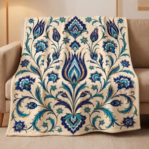 May include: A cream-colored throw blanket featuring a symmetrical floral pattern in shades of deep blue, turquoise, and gold. The design consists of stylized tulips and intricate botanical motifs arranged in a repeating, ornate vertical layout.