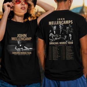 May include: A black t-shirt featuring John Mellencamp's Dancing Words Tour graphics. The front displays the artist playing guitar with text. The back shows multiple black and white photos of the artist, tour dates, and the text The Greatest Hits.