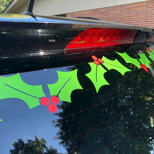 以下が含まれることがあります： リアウィンドウに赤い実のついた緑のホーリーの葉のステッカーが並んだ黒い車