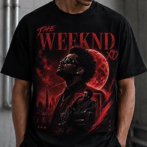 May include: A black short-sleeve t-shirt featuring a graphic print of The Weeknd in red and black tones. The design includes the text THE WEEKND XO, a large red moon, a city skyline, and a smaller image of the artist sitting in a chair.