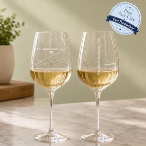 May include: Two clear glass wine glasses featuring etched white map designs of Fredericksburg, Virginia. One glass displays the city name horizontally with a heart icon, while the other features the text Fredericksburg, VA vertically.