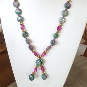 May include: A necklace featuring large, round, green and red gemstone beads interspersed with smaller, faceted pink beads and gold-colored spacers. The necklace is displayed on a white bust.