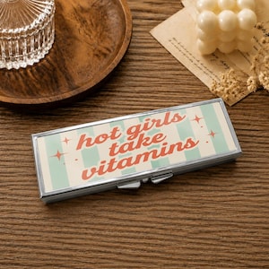 Pode incluir: Uma caixa de comprimidos retangular de metal prateado com um fundo de riscas verticais verde-claras e brancas, com o texto vermelho "hot girls take vitamins" impresso na tampa, decorado com pequenas estrelas vermelhas de quatro pontas.
