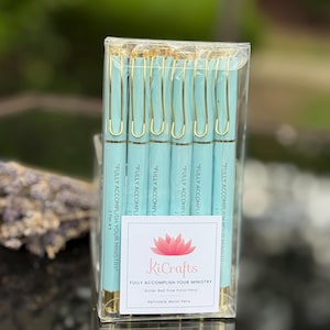 May include: A set of teal rollerball fine point pens with gold-colored clips, packaged in a clear box. The pens have the text "FULLY ACCOMPLISH YOUR MINISTRY" printed on them. A label with the KiCrafts logo and product details is visible.