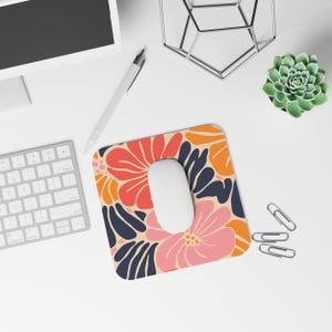 May include: A floral mousepad with a white mouse on top. The mousepad features a beige background with large, colorful flowers in shades of pink, orange, and navy blue. A computer keyboard, pen, and succulent are also visible.