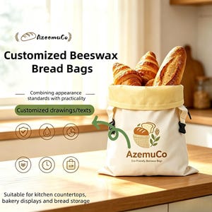 K&ouml;nnte beinhalten: Ein cremefarbener Bienenwachs-Brotbeutel mit gelbem oberen Rand, der das braune Logo 'AzeemuCo Eco-Friendly Beeswax Bags' und eine Grafik von Brot in einem Sack zeigt. Der Beutel ist mit zwei Croissants und einem Baguette gef&uuml;llt, mit Text.