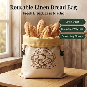 May include: A beige reusable linen bread bag filled with several loaves of bread. The bag features a brown graphic print of a strawberry and a croissant with the text Fruit Bakery. It includes a yellow interior, a drawstring closure, and a removable wax liner.