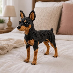 Pode incluir: Uma figura de cão feita à mão em croché com um padrão de cor preta e castanha. O brinquedo tem orelhas pontiagudas erguidas, uma cauda curta e olhos de plástico escuro. A textura do fio é visível em todo o corpo, mostrando o ponto detalhado da forma canina de pé sobre quatro patas com patas e focinho castanhos.