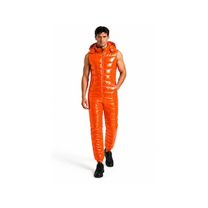 Pode incluir: Um macacão de peça única em laranja brilhante, sem mangas e com capuz, apresentando um acabamento acolchoado de alto brilho estilo puffer com fecho de correr frontal a todo o comprimento. A peça tem uma silhueta ajustada com costuras horizontais.