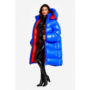 May include: A long, oversized puffer coat featuring a glossy, bright blue exterior and a contrasting vibrant red interior lining. The coat includes a large, padded hood, a full-length front zip, and horizontal quilted stitching throughout the design.